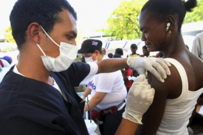 I en flyktningleir i Haitis hovedstad Port-au-Prince gir en cubansk doktor en vaksinasjonssprøyte som del av et WHO-program. 									UN Photo/Sophia Paris
